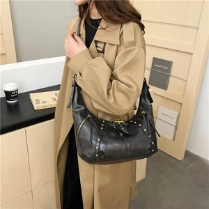 Retro black leather crescent bag with gold rivets and buckle detail on a model