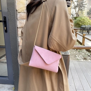 Pink suede envelope crossbody bag with gold chain strap shown on a model outdoors
