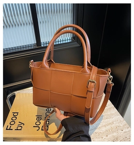 Close-up of brown woven bucket bag featuring large leather weave and round handles