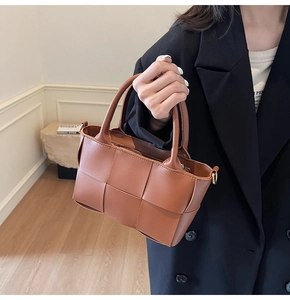 Detail showing the brown woven leather texture and golden metal D-ring of the bucket bag