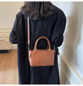 Close-up of brown woven leather bucket bag worn with a black long coat on a model