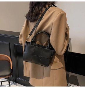Detailed shot of a black woven crossbody bag styled on a camel coat for a chic look