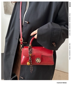 Detail of red glossy leather handbag with gold twist lock and woven bell charm accessory