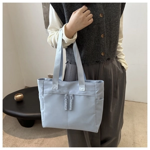 Detail of light blue nylon tote bag showing woven rope zipper pulls and dual front pockets