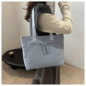 Detail of light blue tote bag featuring nylon fabric and decorative woven rope zipper pull