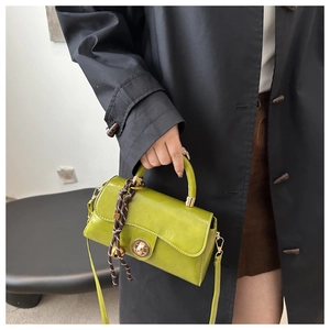 Detail of green glossy crossbody bag with gold twist lock and woven pendant accessory