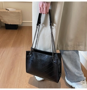 Close-up of black quilted leather shoulder bag with chain strap and V-shaped stitching