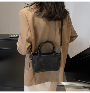 Detail of black woven leather tote bag featuring gold hardware and removable shoulder strap