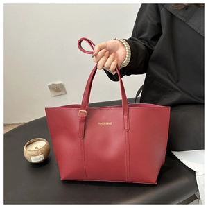 Detail of dark red matte leather tote bag featuring gold hardware and logo text