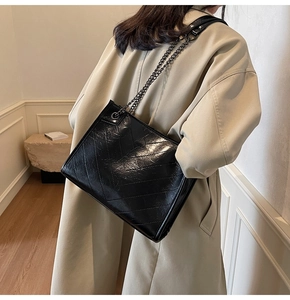Detailed view of black quilted tote bag with chain strap worn over a beige coat