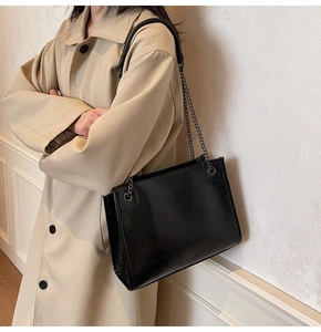 Detail of black V-quilted faux leather tote bag with metal chain strap on model