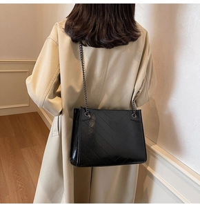 Detail of black quilted leather tote bag with metal chain strap on model shoulder