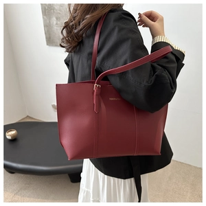 Detail of dark red faux leather tote bag with gold lettering and adjustable straps