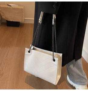 Detail of white leather tote with V-quilted stitching and metal chain strap on model
