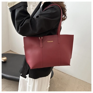 Model wearing a burgundy minimalist tote bag with thin straps and gold lettering