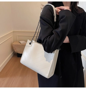 Detail of white quilted tote bag with black chain strap on model in modern interior