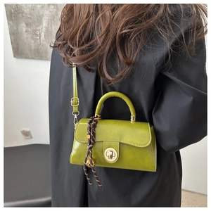 Detail of matcha green handbag with gold lock and striped rope charm on black coat