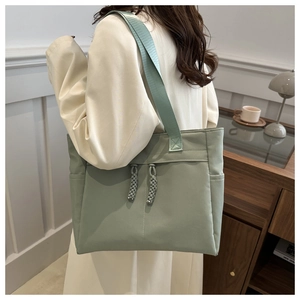 Detail view of a pale green nylon tote bag featuring stylish woven knot decorative tassels