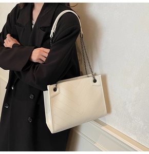 Detail of V-quilted cream tote bag featuring black metal chain strap and leather pad