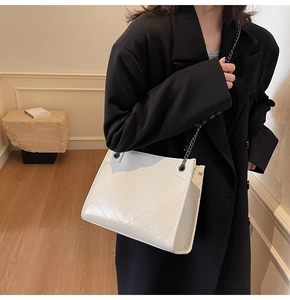 Detail of cream V-quilted faux leather tote with dark grey metal chain on black coat