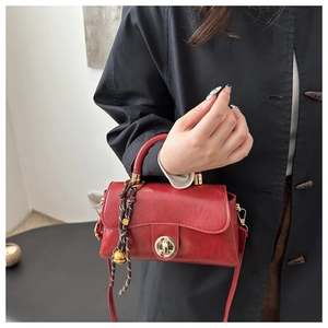 Detail view of red leather crossbody bag with gold twist lock and woven charm detail