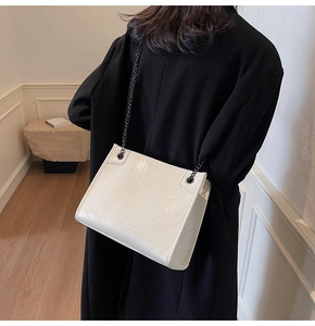 Close-up of white crossbody bag with V-shaped quilting and black metal chain strap on model