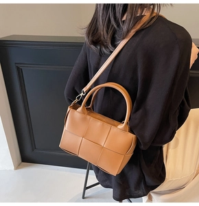 Detail of woven brown leather handbag showing intricate texture and metal strap clasp