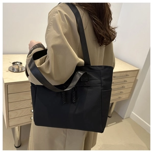 Side view of black nylon tote bag with wide straps on model in khaki trench coat