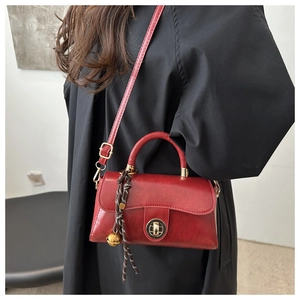Detail of red leather crossbody bag with golden rotary lock and braided bell charm