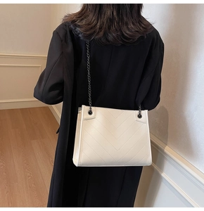 Close-up of white quilted tote bag with V-shaped stitching and dark grey metal chain