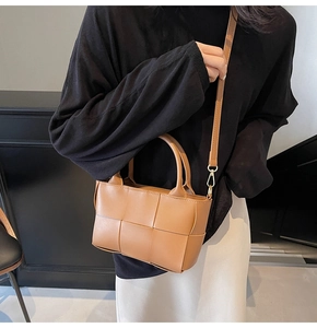 Detail of a brown woven bucket bag with wide leather strips and golden metal hardware