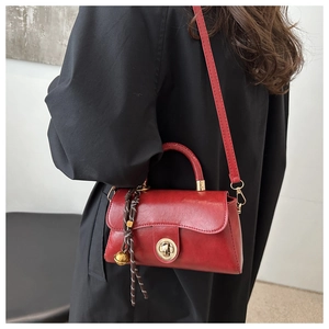 Detail of red vintage matte leather handbag with golden twist lock and woven charm