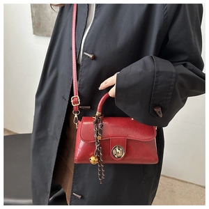 Detail of red patent leather mini handbag with gold clasp and decorative bell charm