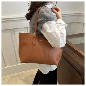 Detail of adjustable golden buckle and smooth leather texture on a brown tote bag