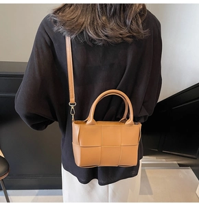 Rear view of model showing brown woven bucket bag with top handles and shoulder strap