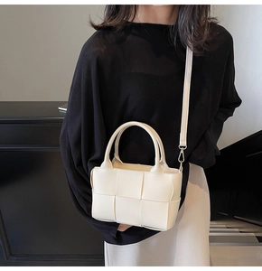Detail of an off-white woven tote bag with a dual-handle design and a thin shoulder strap