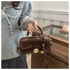 Dettaglio borsa in pelle marrone scuro con chiusura a rotazione dorata e ciondolo intrecciato
