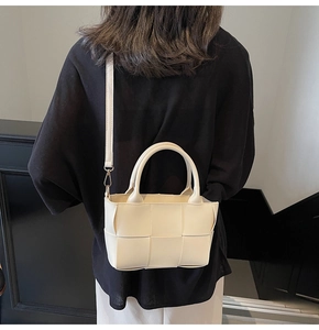 Detail of cream woven tote bag showing the wide weave texture and removable shoulder strap