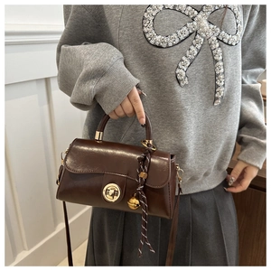 Detail of vintage brown leather handbag featuring a gold rotary lock and decorative charms