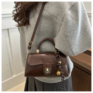 Detail of dark brown vintage faux leather handbag with gold lock and sphere charm accessory