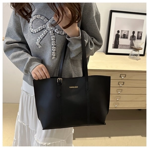 Detail of black faux leather tote with golden text and slim straps in cozy indoor setting
