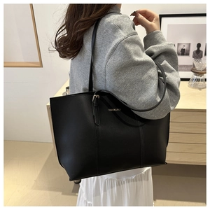 Side view of a minimalist black leather tote bag with gold lettering shown on a model