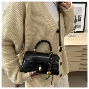 Detail of vintage black oil wax leather handbag with gold lock and bell charm on model