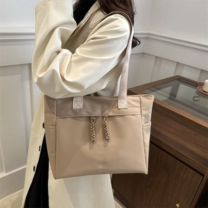 Minimalist beige nylon tote bag with dual front zippers shown in a modern interior