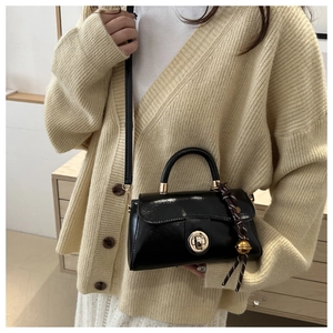 Detail of a black glossy patent leather crossbody bag with a round gold twist lock