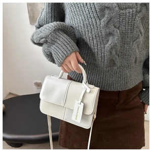 Detail of white two-tone square crossbody bag held by model with elegant metal tag