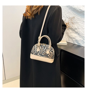 Detail of leopard print shell bag with beige leather handles and dual metal zippers