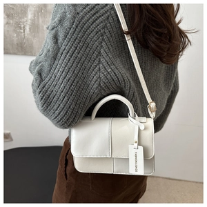 Détail du sac carré bicolore avec poignée supérieure et bandoulière porté par un mannequin