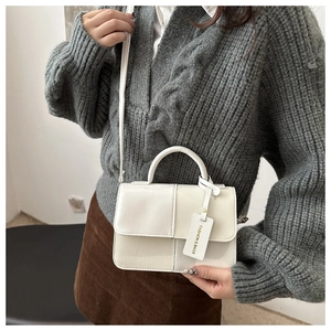Gros plan du sac bandoulière blanc avec textures mixtes et étiquette sur un mannequin