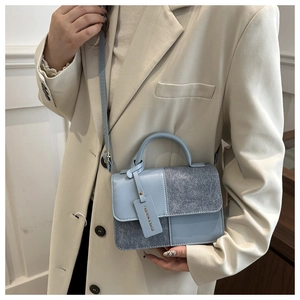 Detail view of light blue crossbody bag with mixed leather textures and fashion tag